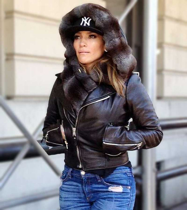 Person wearing a black leather jacket with fur-lined hood and blue jeans, standing outdoors.