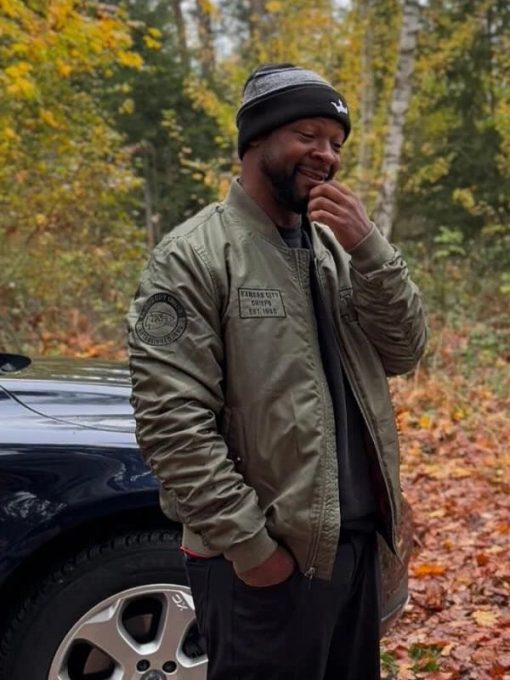 Man in a green jacket standing next to a car in a forest setting